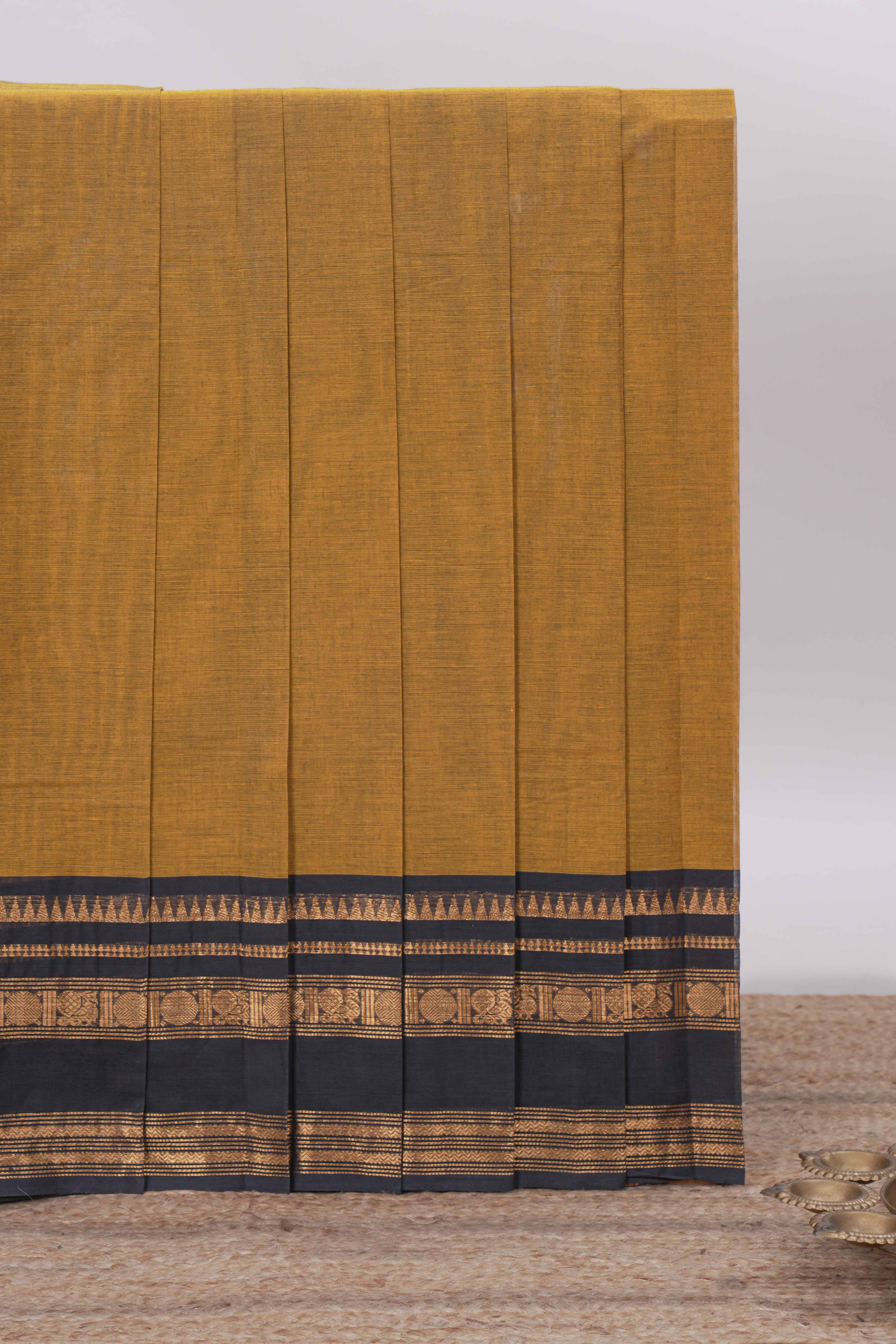 Deep Mustard yellow Chettinad cotton saree with a plain body and a contrasting black border by antique gold zari motifs along with blouse piece