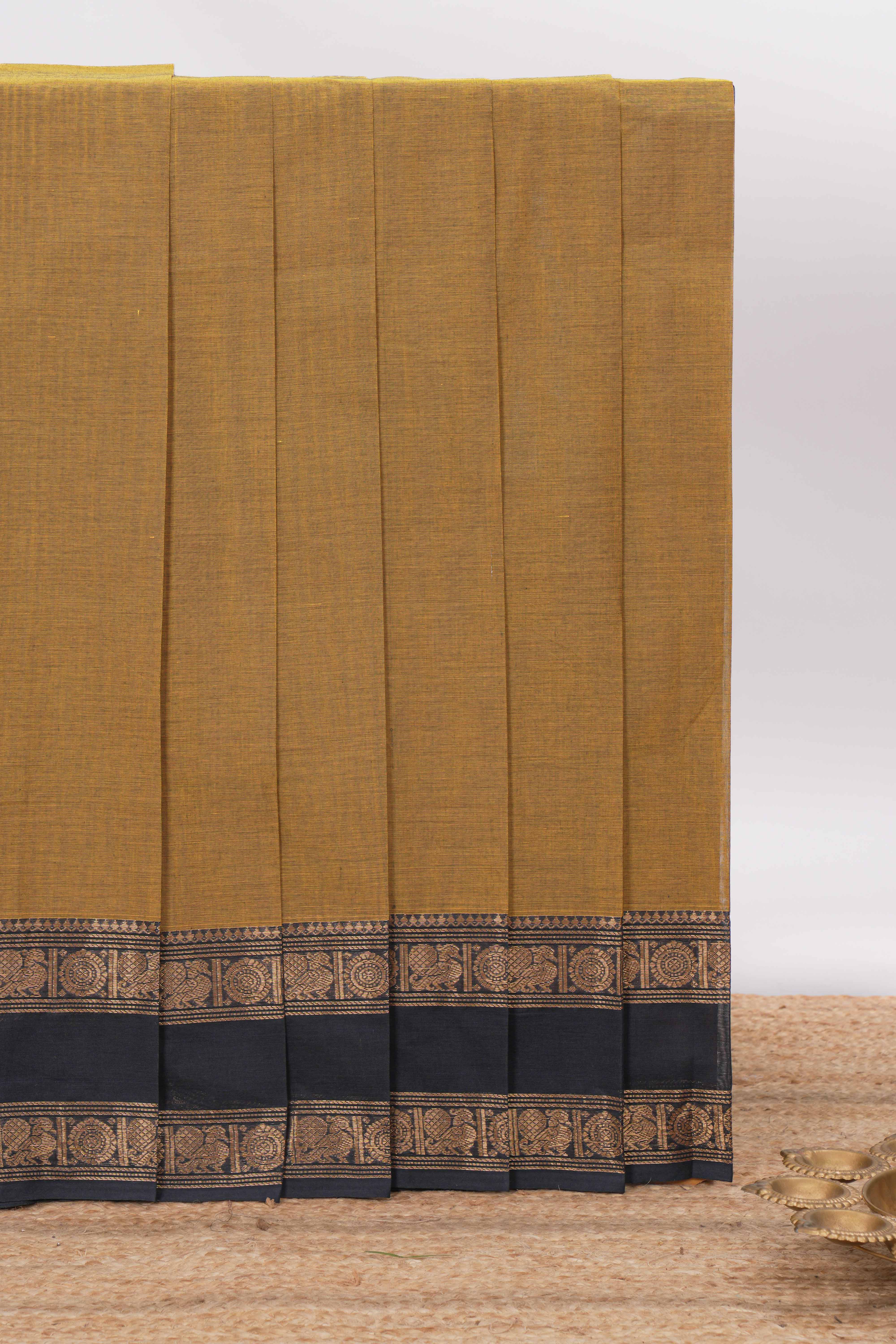 Mustard yellow Chettinad cotton saree with a plain body and a contrasting black border by intricate antique gold zari motifs along with blouse piece