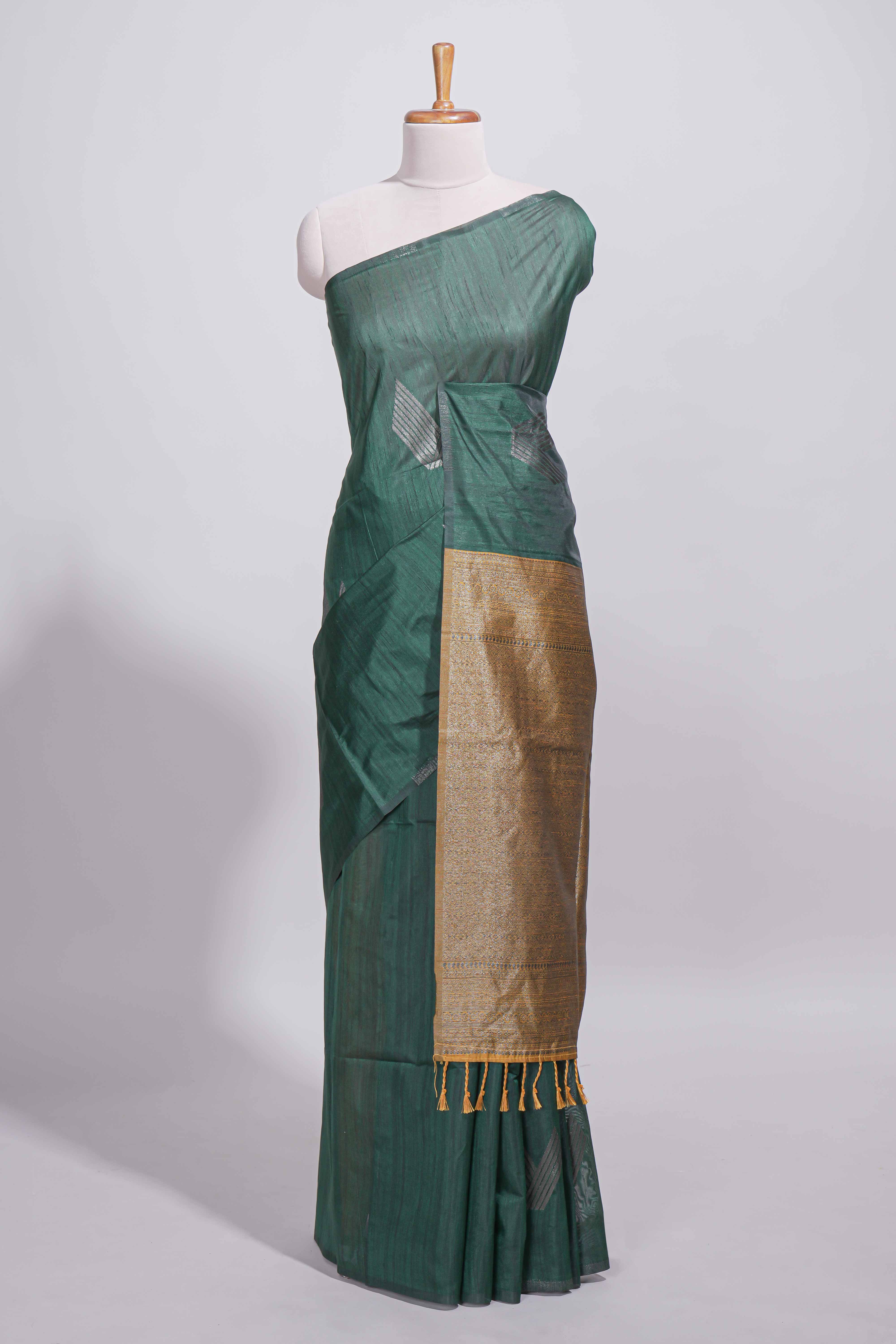 Bottle green tussar saree with subtle silver woven motifs paired with a rich antique gold zari pallu with tassels with contrast blouse piece