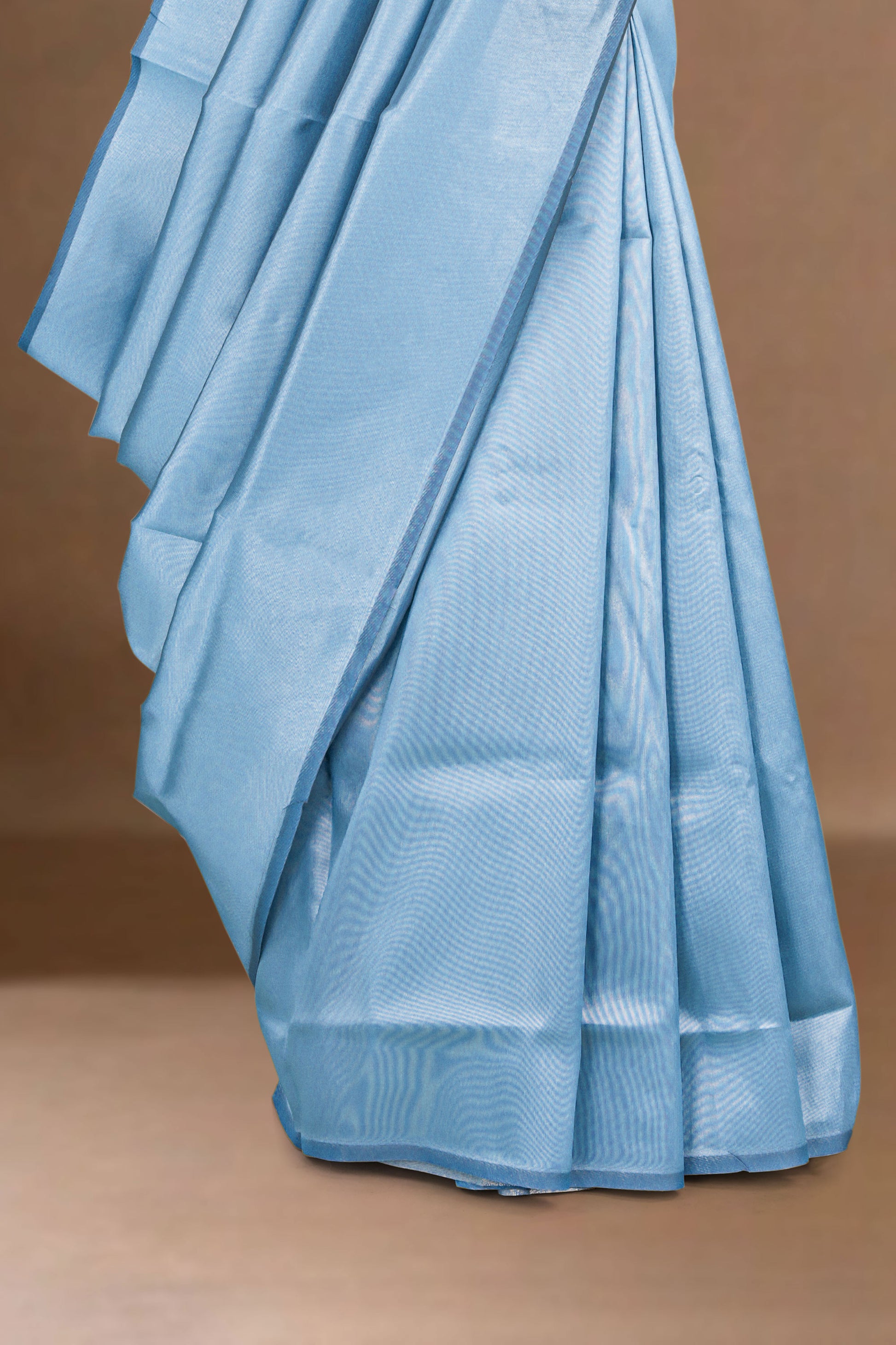 Light blue lichi silk saree with a subtle pattern on a brown background