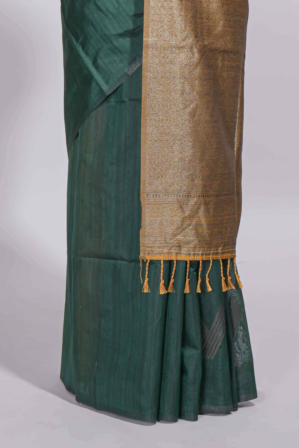 Bottle green tussar saree with subtle silver woven motifs paired with a rich antique gold zari pallu with tassels with contrast blouse piece