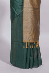 Bottle green tussar saree with subtle silver woven motifs paired with a rich antique gold zari pallu with tassels with contrast blouse piece